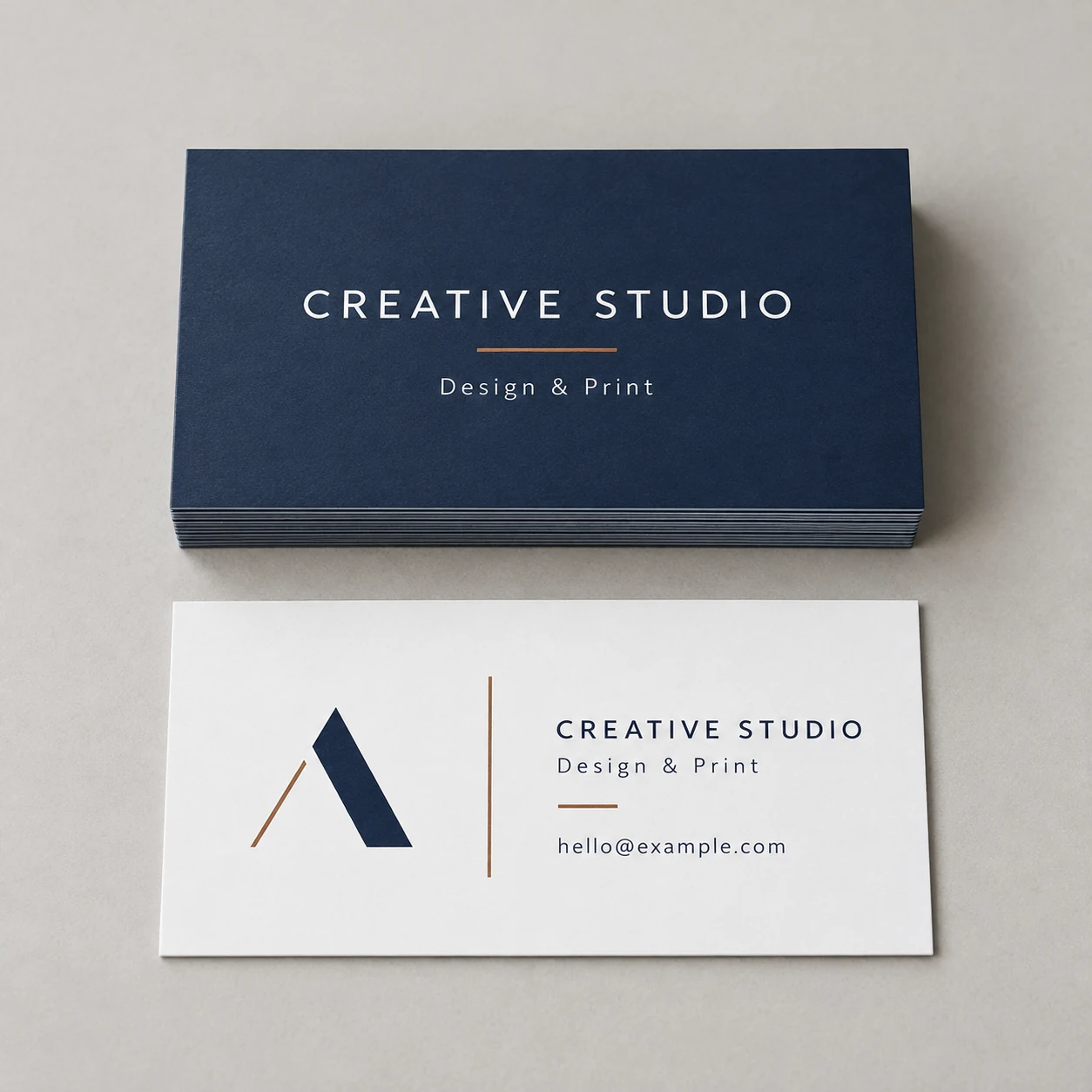 Printed design-studio business cards with navy lettering and a copper-colored accent photographed on a light studio surface